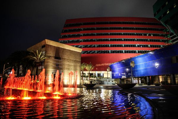 A wide shot of a sparsely attended conference-style event in an upscale Los Angeles venue, empty chairs visible, boxed lunches on tables, the kind of aspirational space that signals presti...