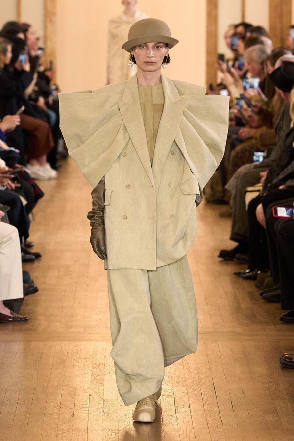 A runway shot from Uma Wang's Fall 2026 collection showing one of the architectural, textural pieces — ideally the opening charcoal coat or another look that demonstrates the unstructured,...