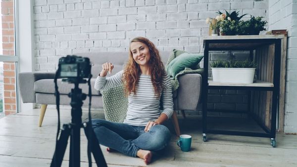 Woman waves at camera while recording video at home.