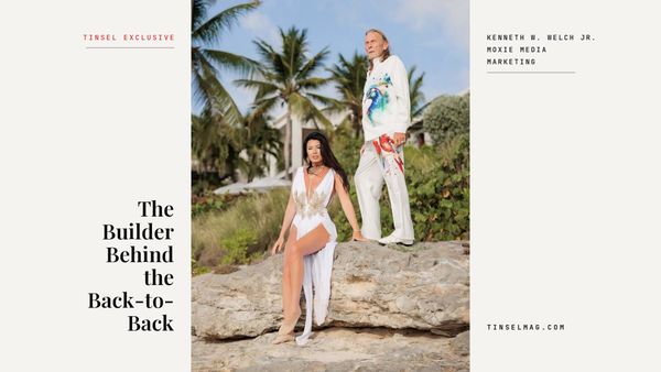 Kenneth W. Welch Jr. stands on a beach rock in a white painted suit beside Jolene Burns, seated in a white gown, on a warm white cover with the line The Builder Behind the Back-to-Back