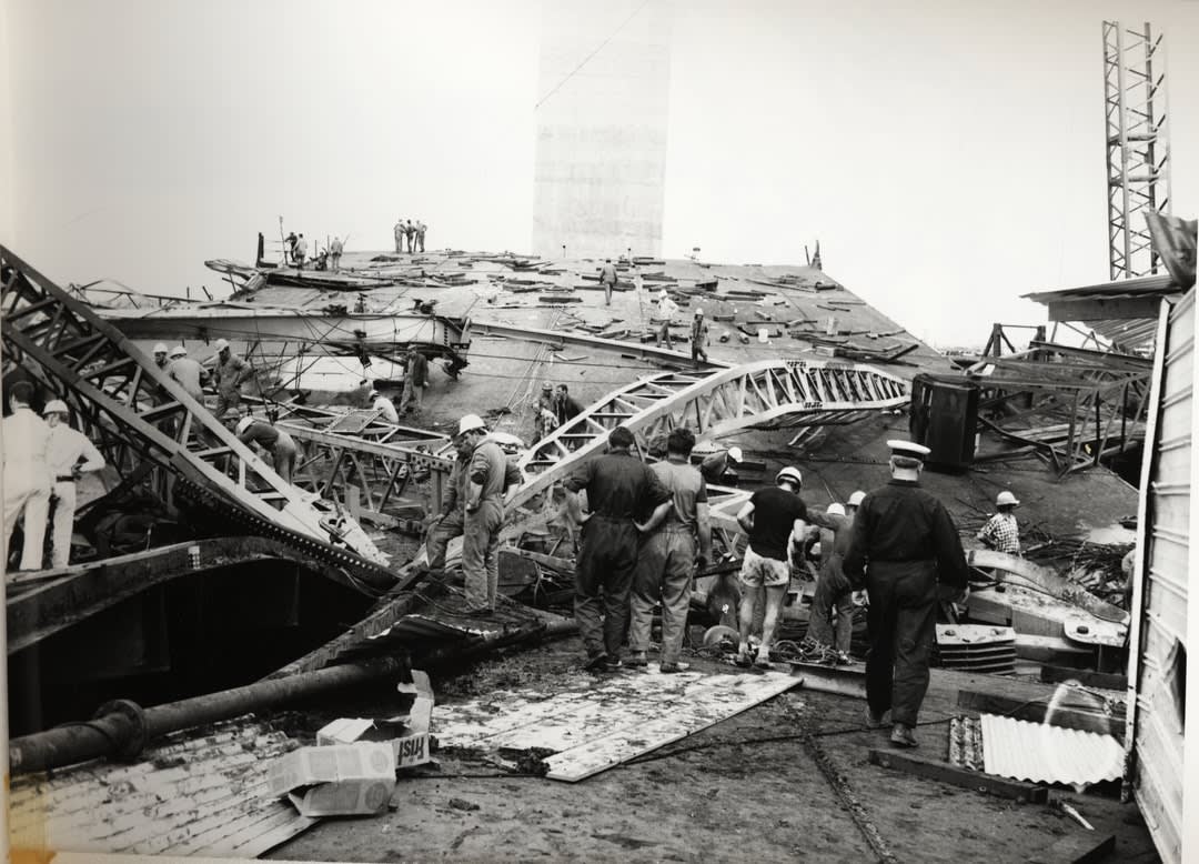 Rescuers and workers stand around the twisted girders of the West Gate Bridge.