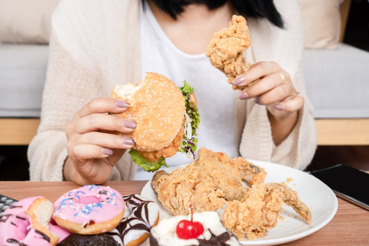 Unhealthy woman over eating fast food burgers, fired chicken, donuts, and desserts