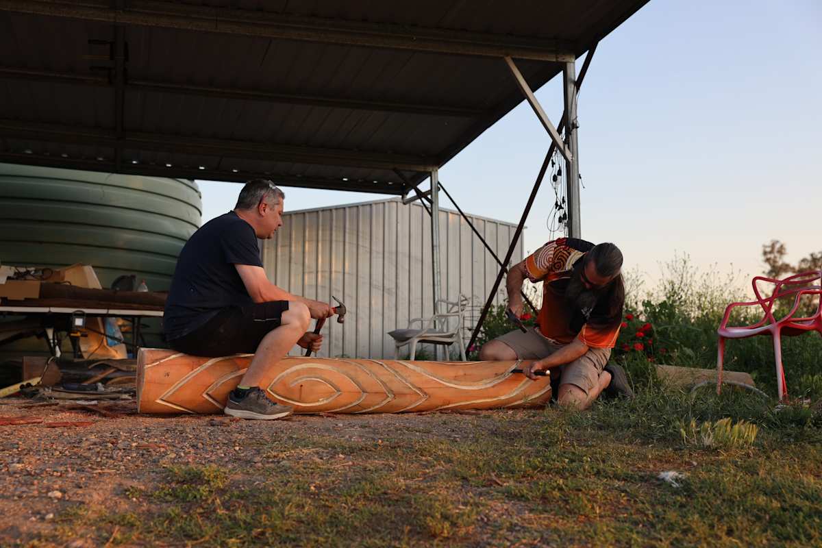 Two men carving designs into a tree trunk laying on the ground