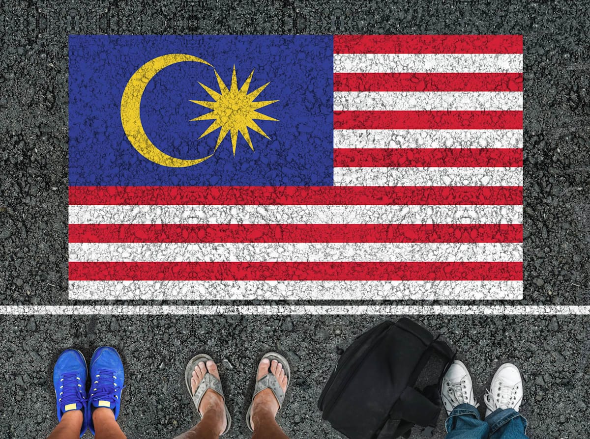 Legs standing on asphalt road next to flag of Malaysia and a border line