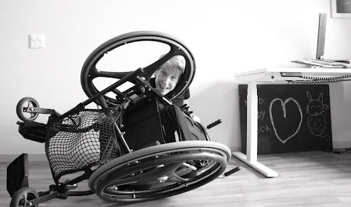 A smiling Dr Melinda Smith peering through a gap in her overturned wheelchair – black and white image