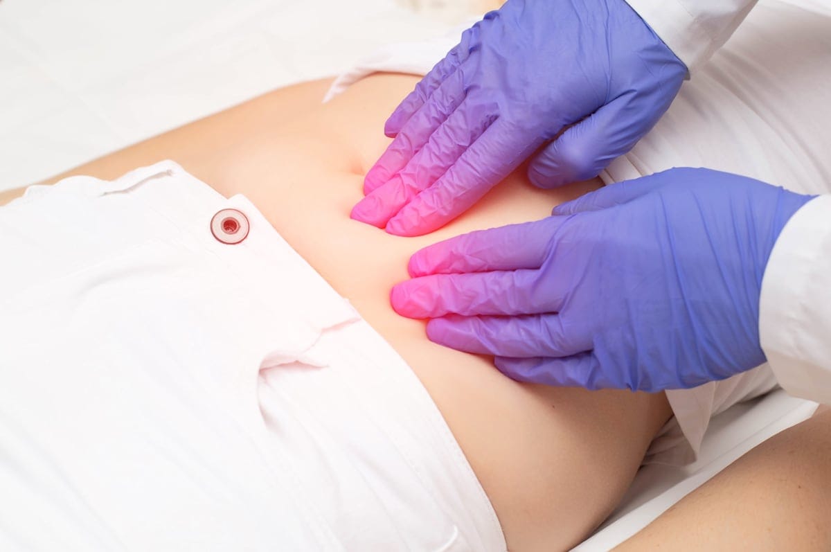 A doctor wearing blue gloves probes the lower abdomen of a female who has pain and inflammation of the reproductive system