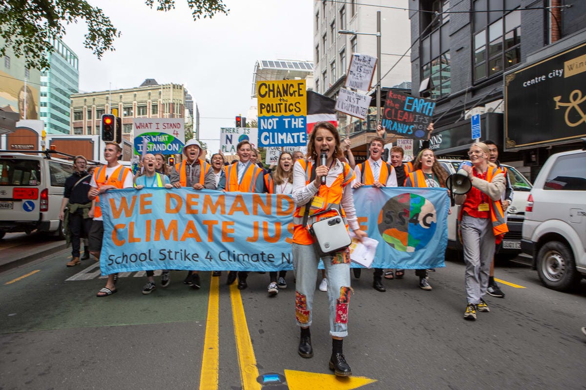 A yound woman with a microphone leads student marchers with banners in a School Strike 4 Climate protest in Wellington, New Zealand