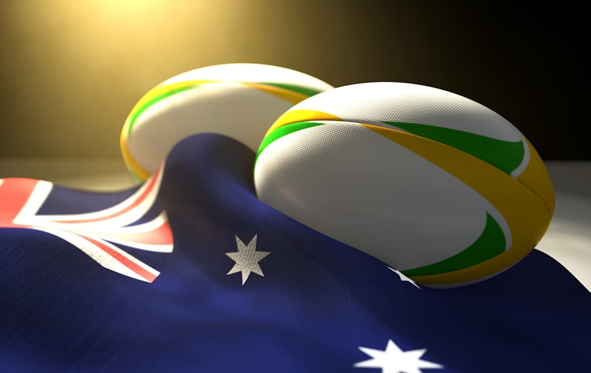 Two regular rugby balls with colour design elements resting on a draped Australia flag 