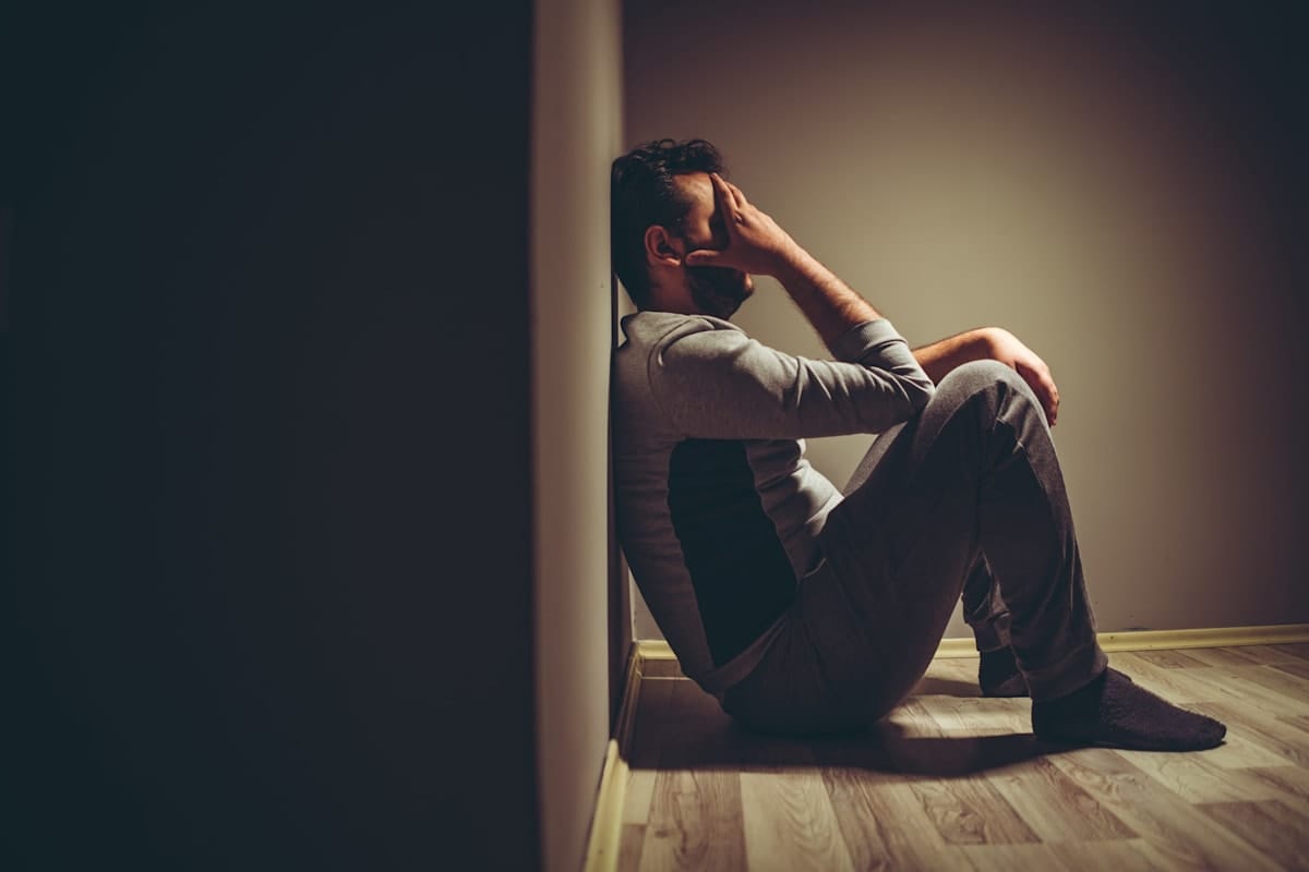 Stressed man sitting against a wall holding his hand to his head