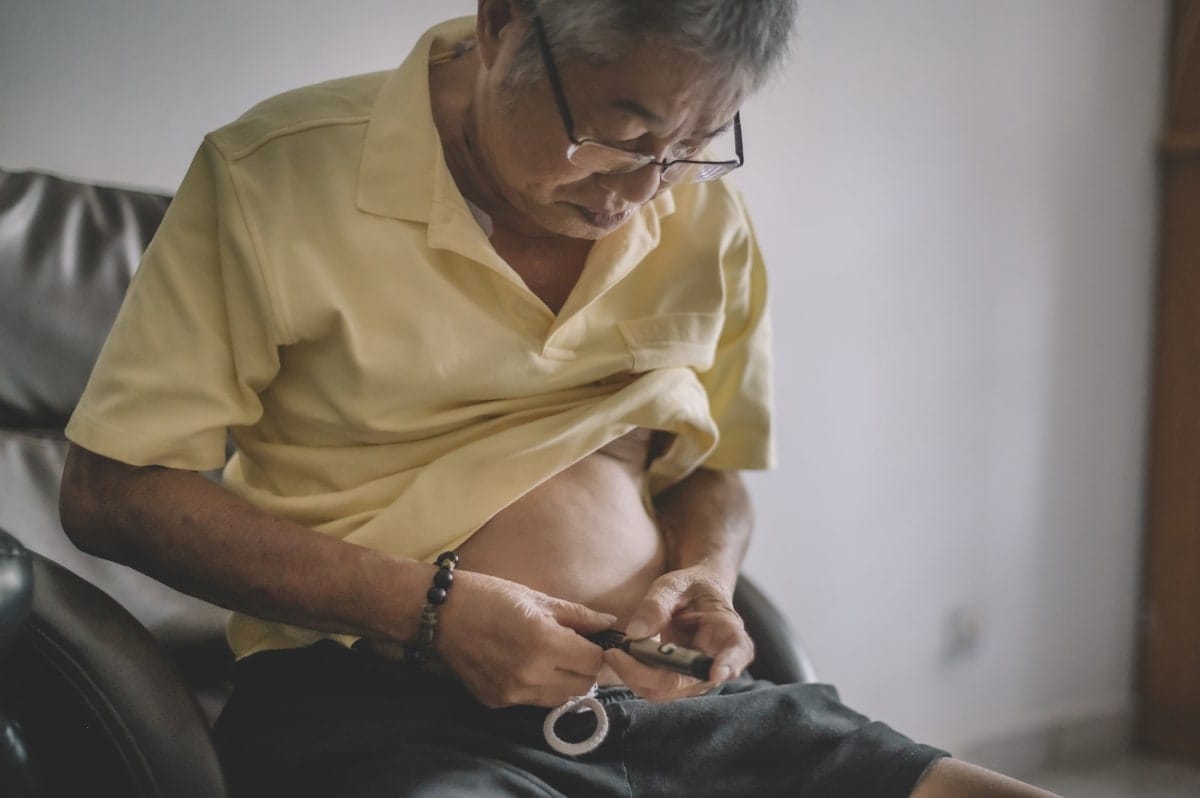 Older Asian man injecting insulin injection into his stomach