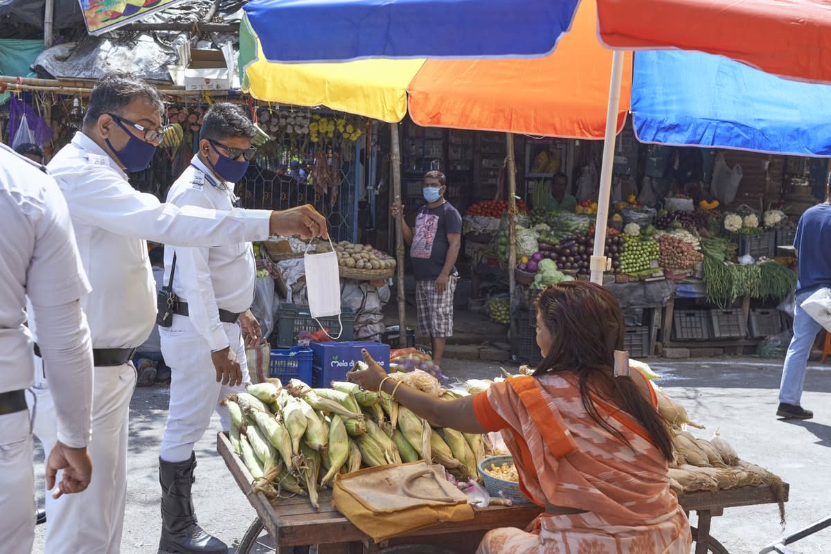 A woman street vendor in India is handed a mask by one of a group of three male officials