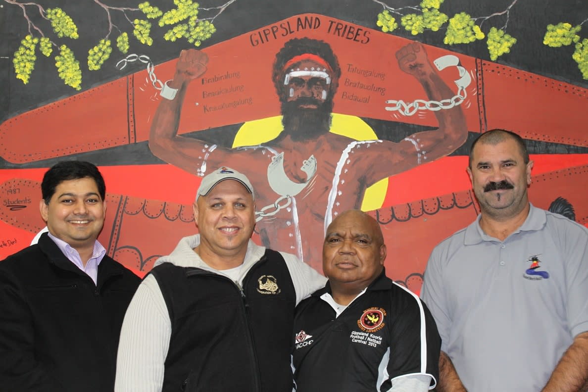 Dr Anton Isaac with three community collaborators in front of an Indigenous mural bearing the words 