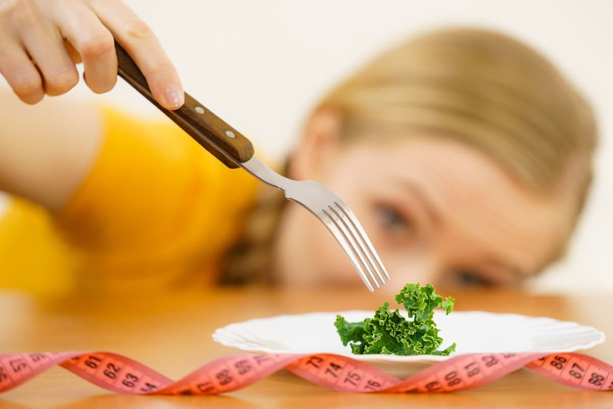 young blonde woman dealing with anorexia nervosa or builimia having small green vegetable on plate.