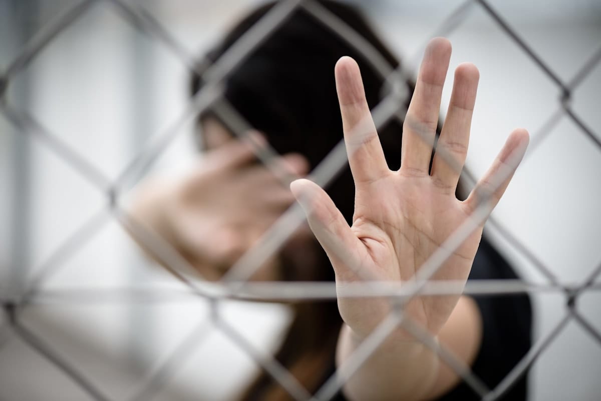 Blurred woman holding her hand up against a chain-link fence