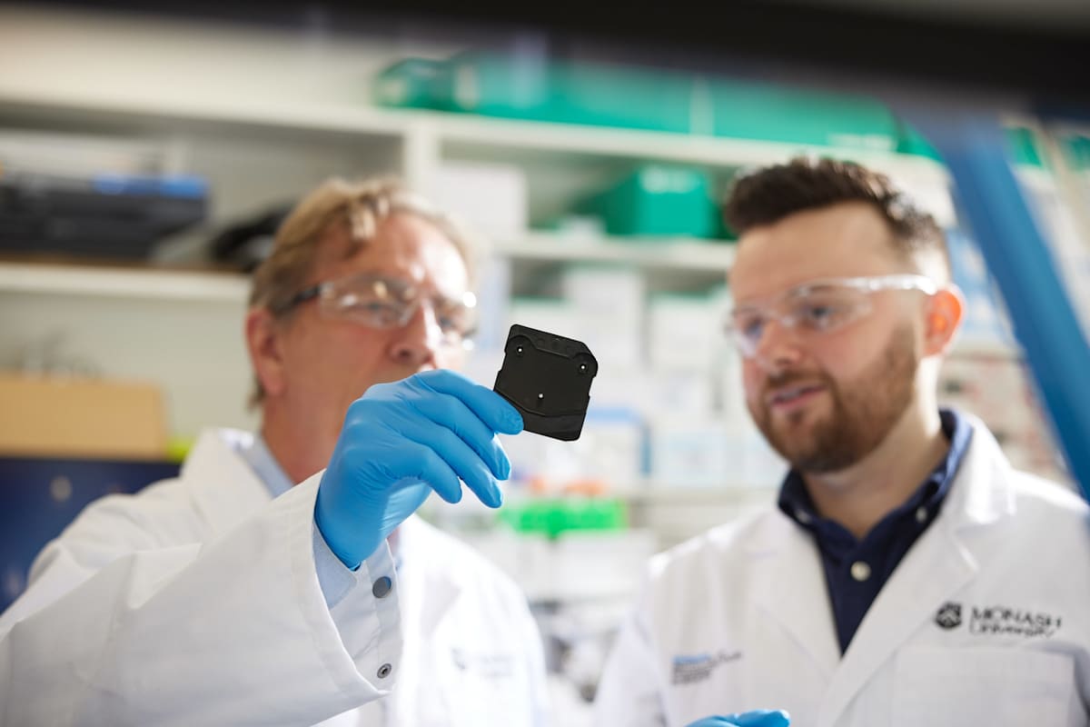 Professor Colin Pouton holds a micromixer chip, with PhD student Thomas Payne looking on