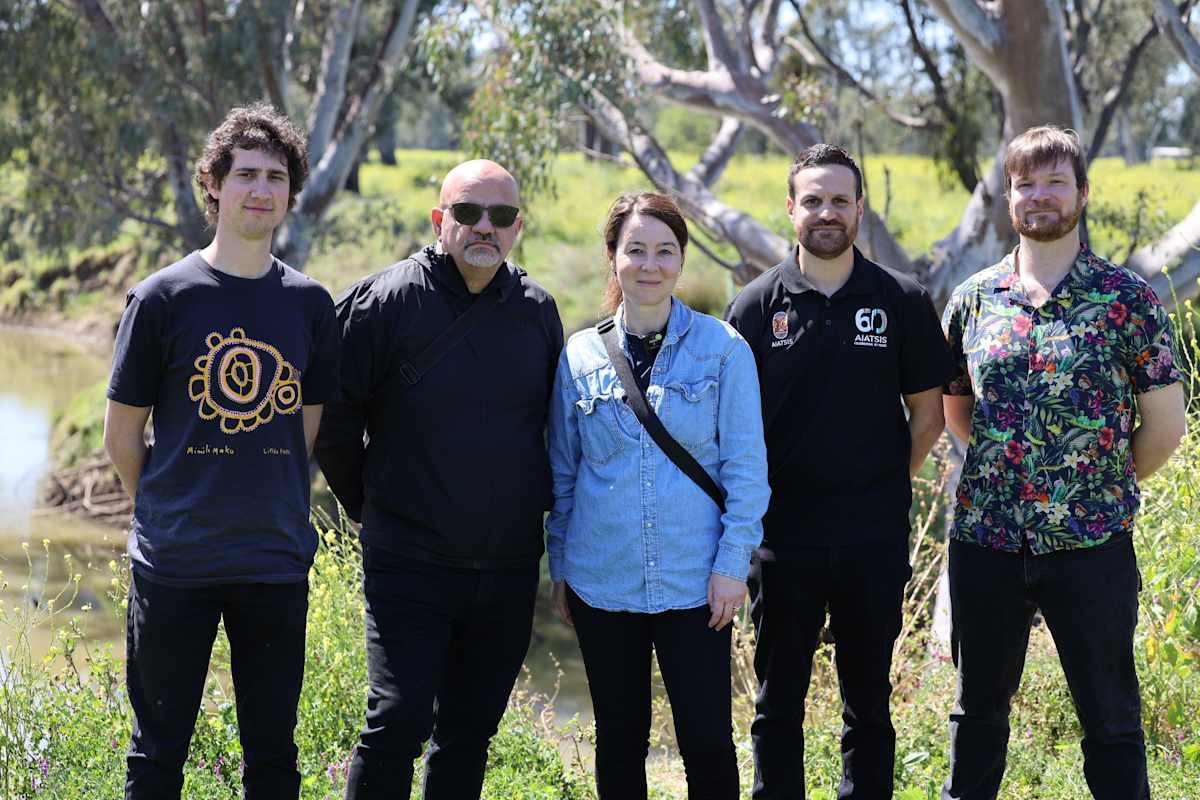 Five people standing with trees in background, facing the camera