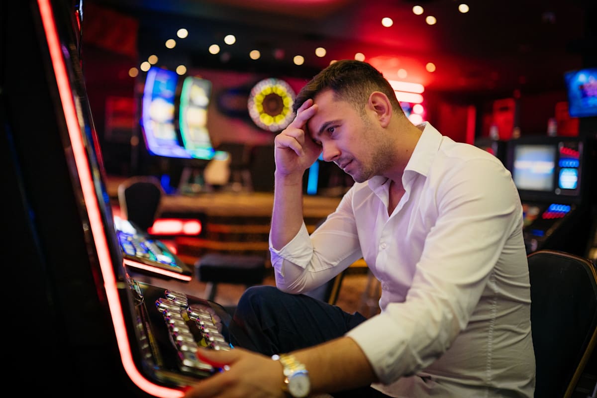A depressed young man losing his money on a pokier machine