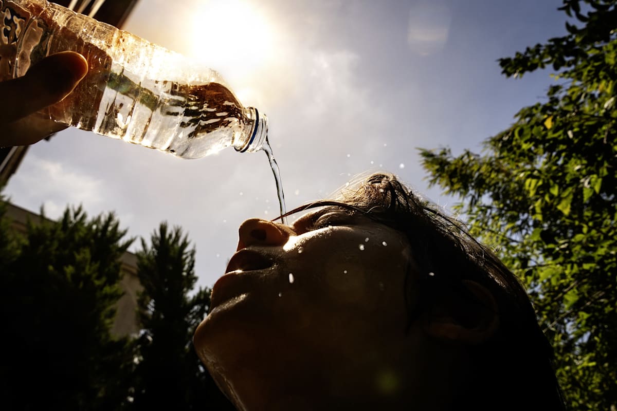 Woman pouring water from bottle on her face to cool down during hot summer day