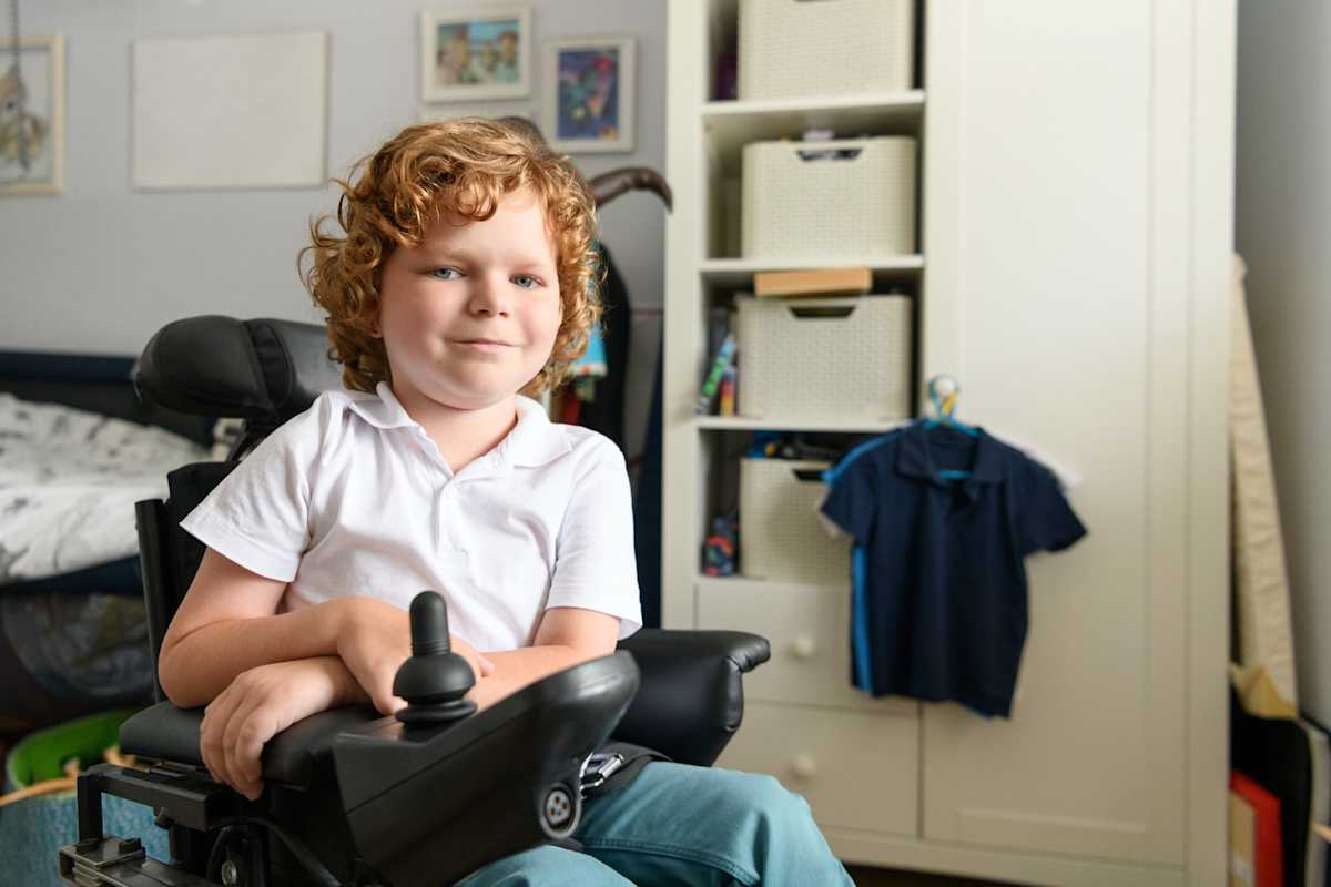 oung disabled boy in powered wheelchair in bedroom smiling