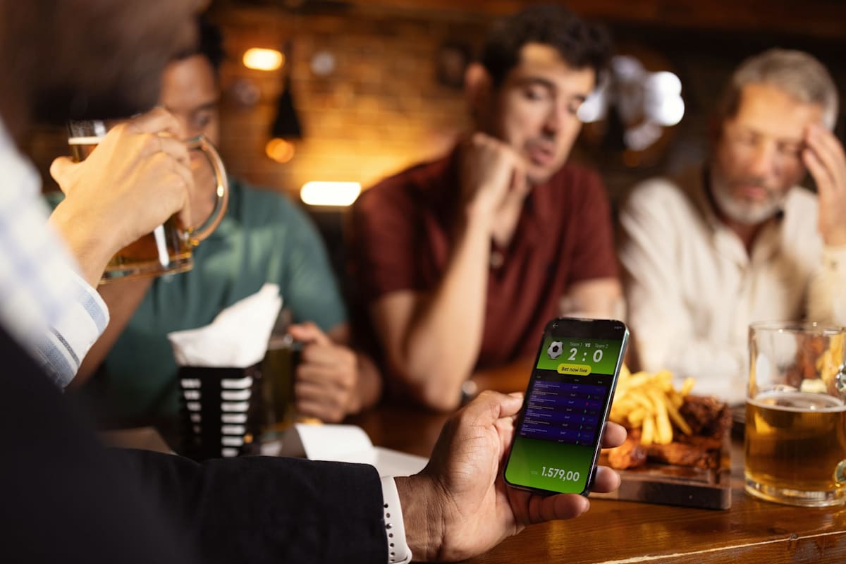 Close-up shot of an unrecognisable man holding smartphone and watching the sports match results, while watching the game with a group of friends in the pub
