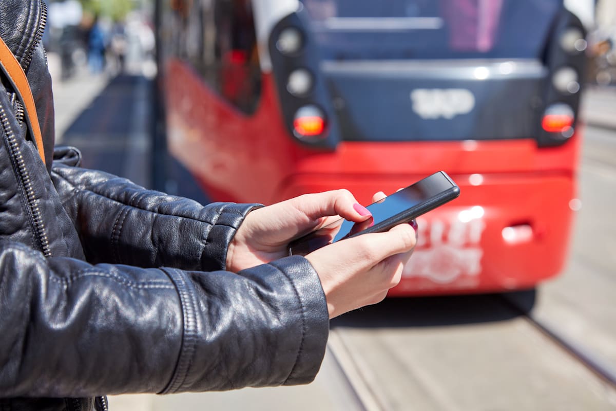 Commuter lookinig at phone in front of tram.
