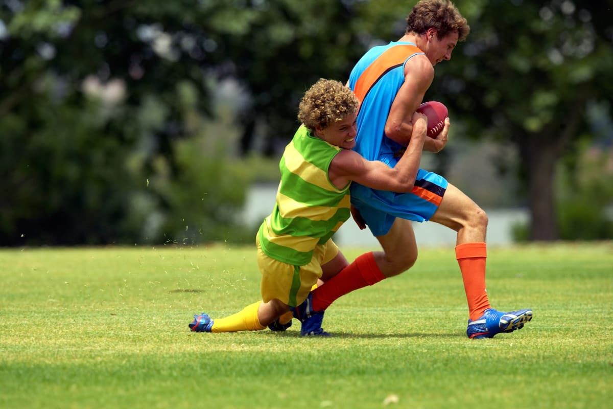 Football player tackling an opposition player on an oval.