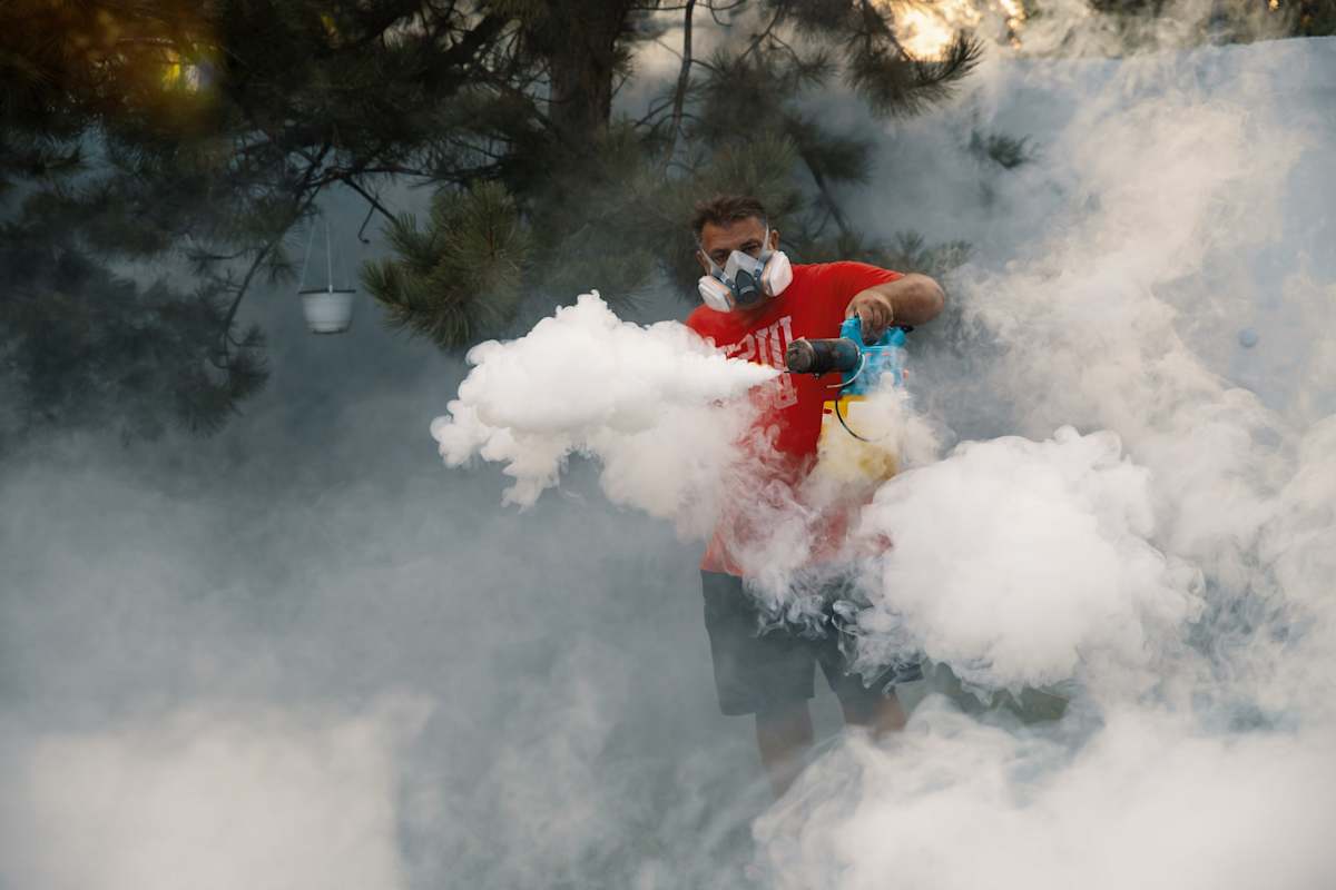 Man in protective mask using fumigation machine to kill mosquitoes