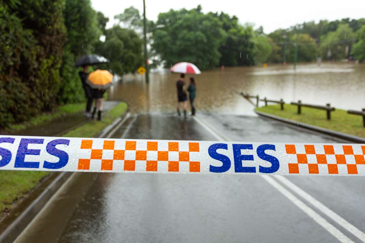 Emergency services tape across a flooded road with people standing at the water