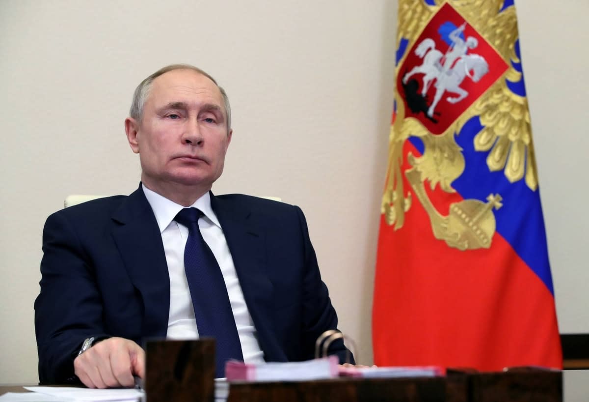Russian President Vladimir Putin sitting at a desk with the Russian flag in the background