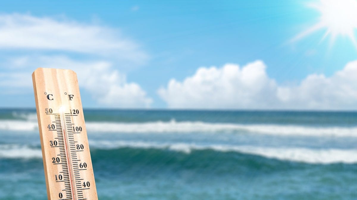 Thermometer stuck in the sand at the beach with the ocean in the background