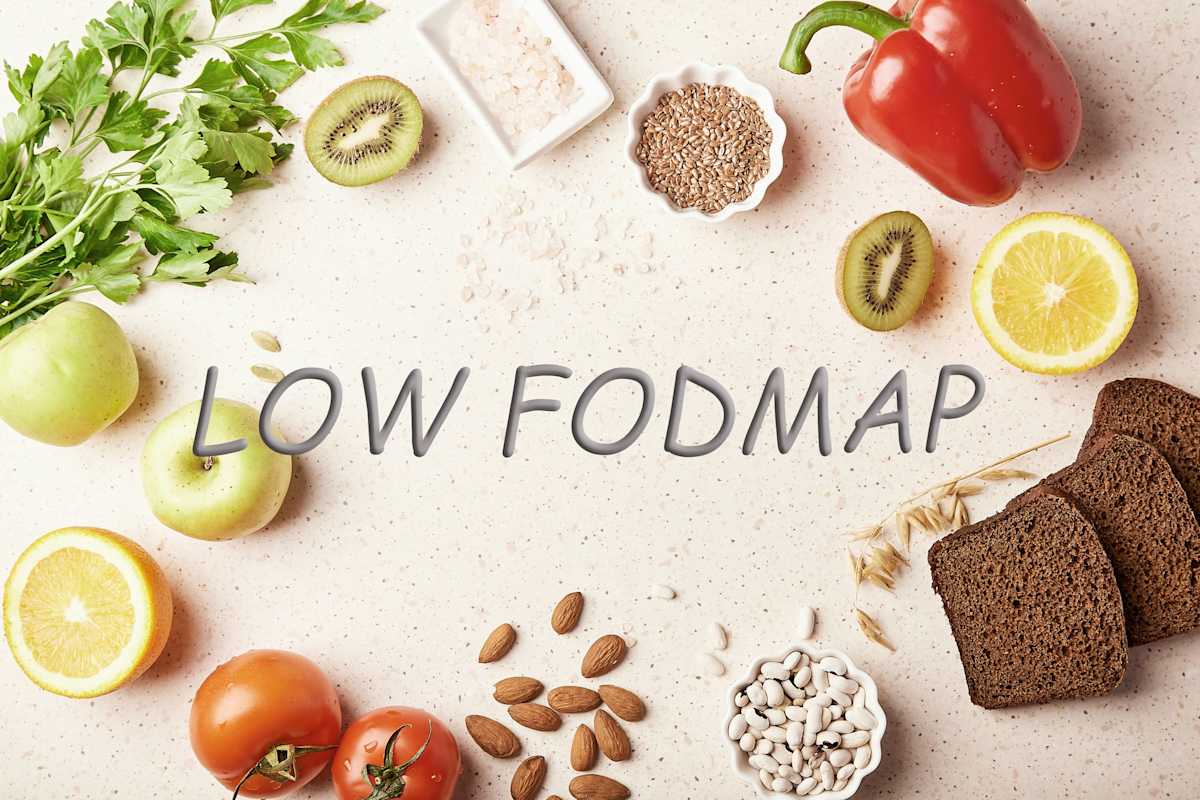 Low FODMAP concept with text in centre, surrounded by fruits, vegetables, greenery, nuts, beans, flax seeds, chia seeds, wholegrain bread. 
