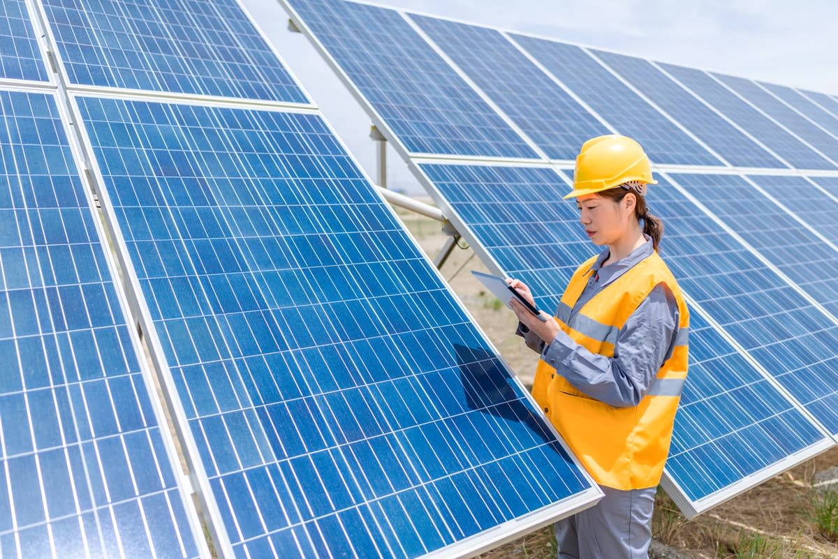 A Chinese woman engineer works on an iPad while standing next to a solar pane.