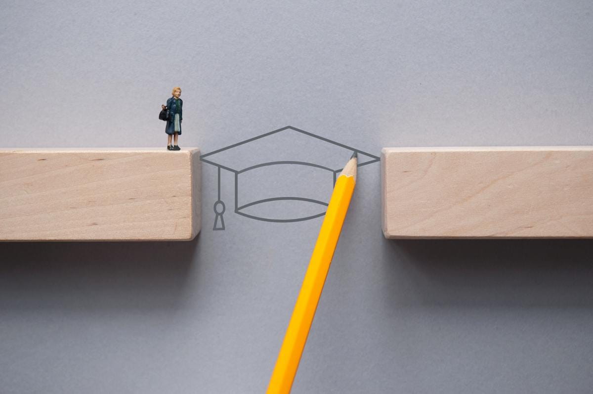 Academic cap bridges the divide between two blocks, allowing figurine to step across.