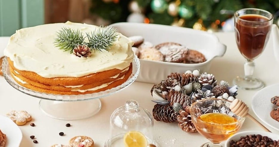 Christmas cake and sweets on table, with Christmas decorations in the background.