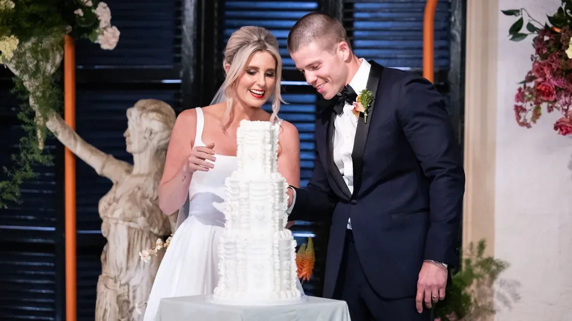 a bride and groom smiling as they look at a wedding cake