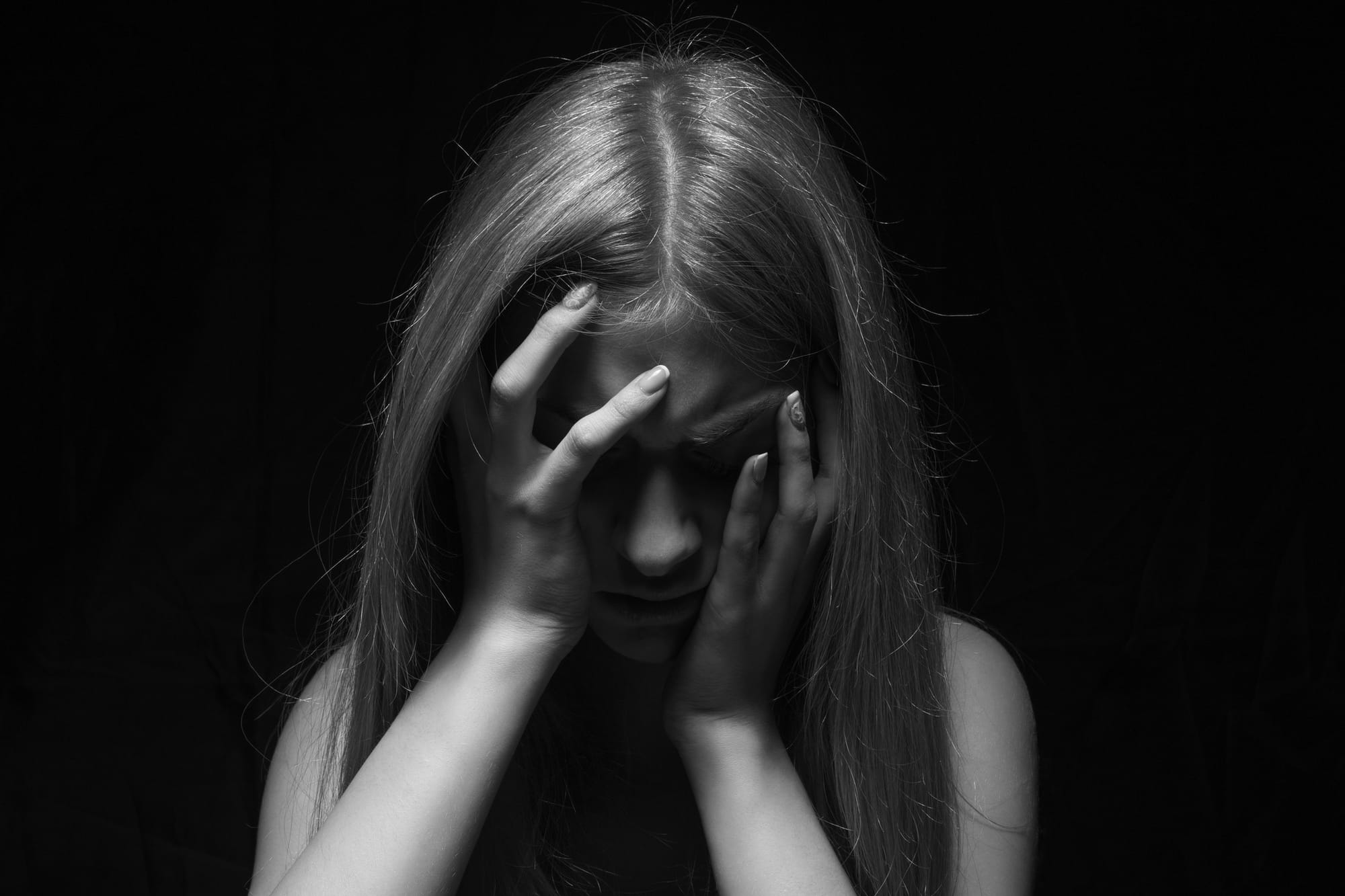 Black and white photo of an obscured woman with her head in her hands in pain.