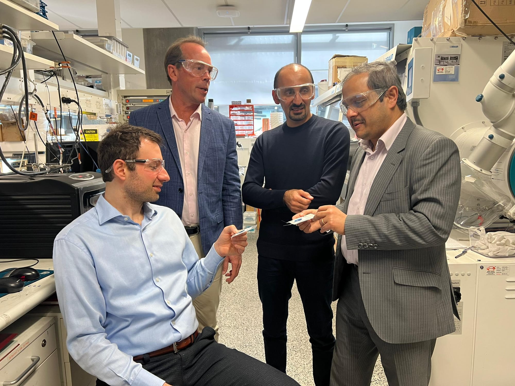 Four researchers wearing eye protection in a lab examining a supercapacitor