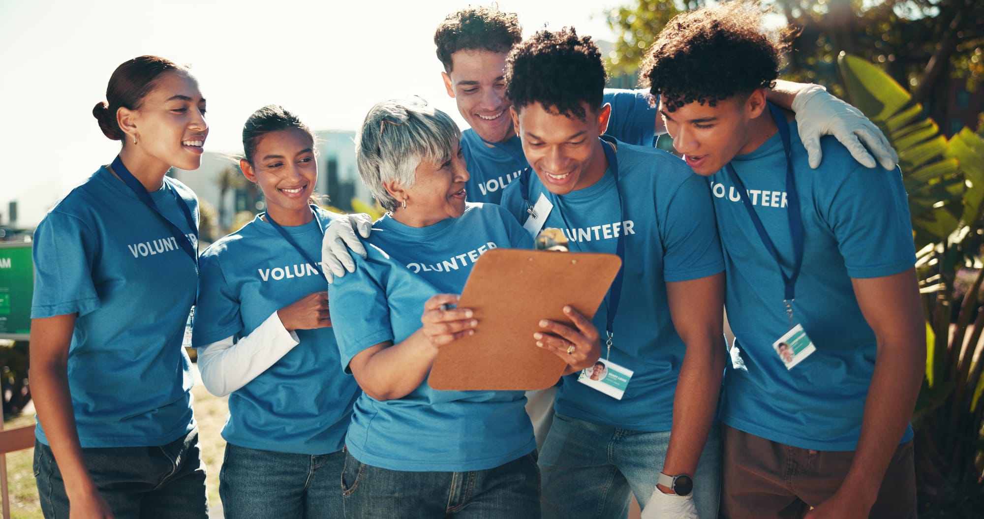 A group of smiling volunteers gathered around a woman with a clipboard.