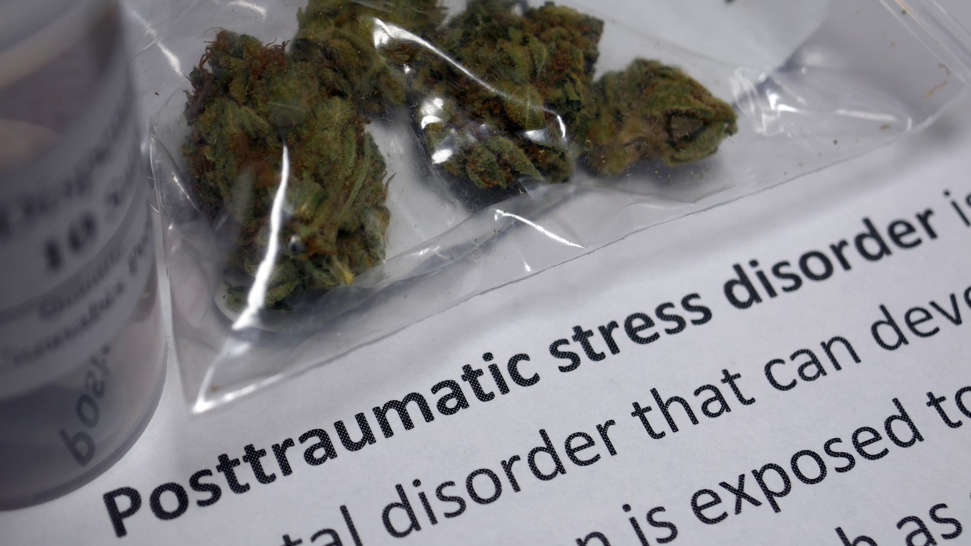 Cannabis flower buds in a plastic bag sitting on paper with the words Post-traumatic stress disorder written on it.