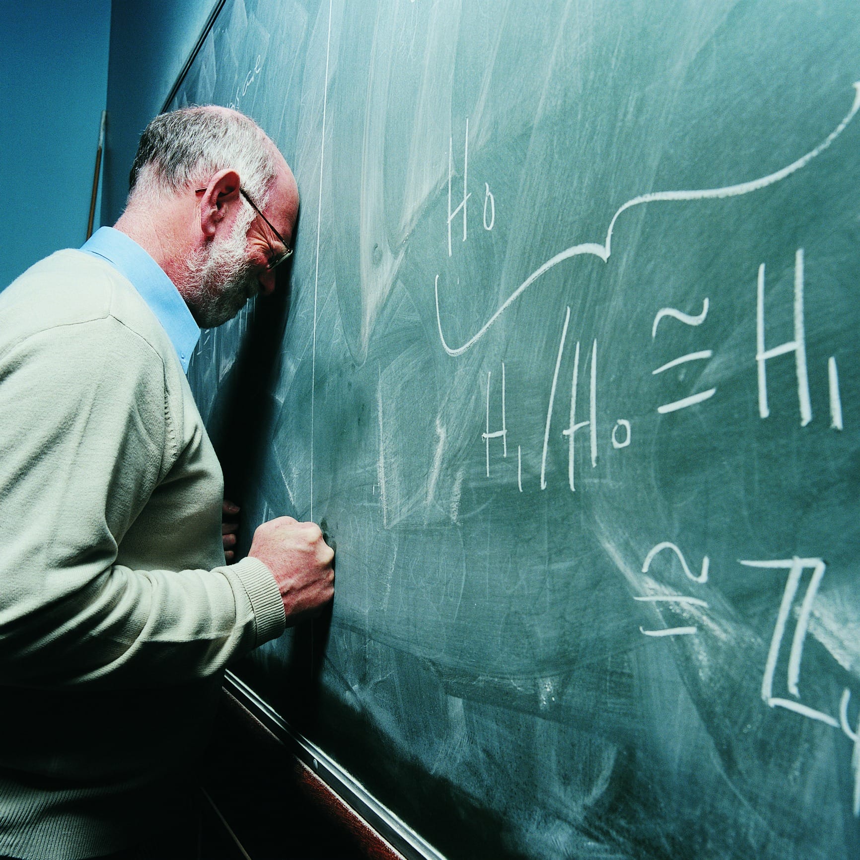 Portrait of a frustrated maths lecturer banging his head against a blackboard.