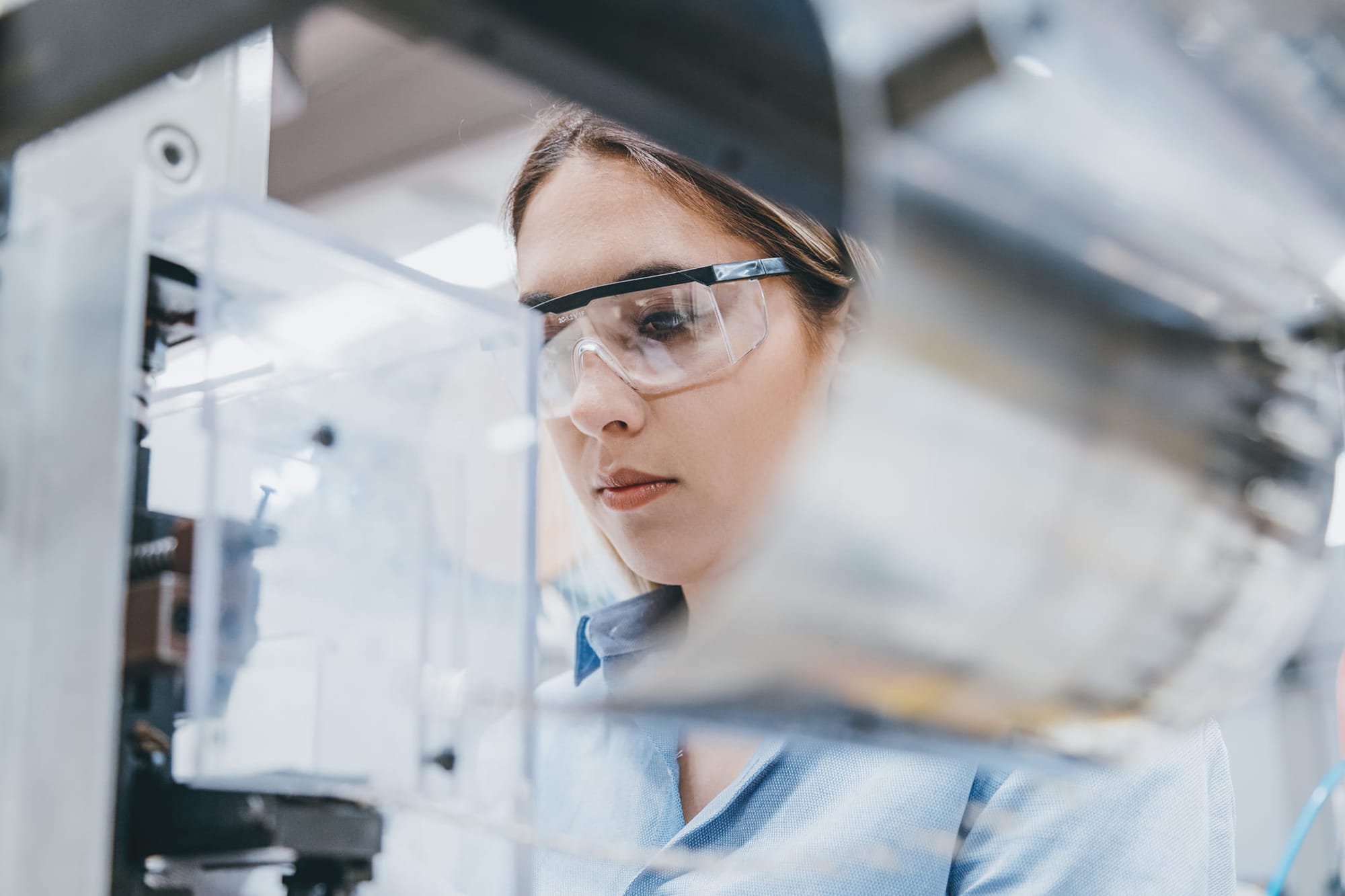 A woman in protective eyeweaer working on equipment in a lab