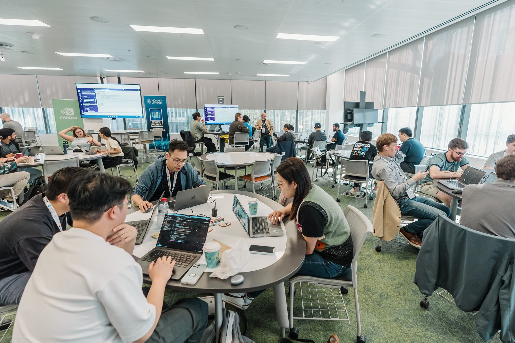 Room filled with people involved in the Hackathon, sitting at desks looking at their computers.