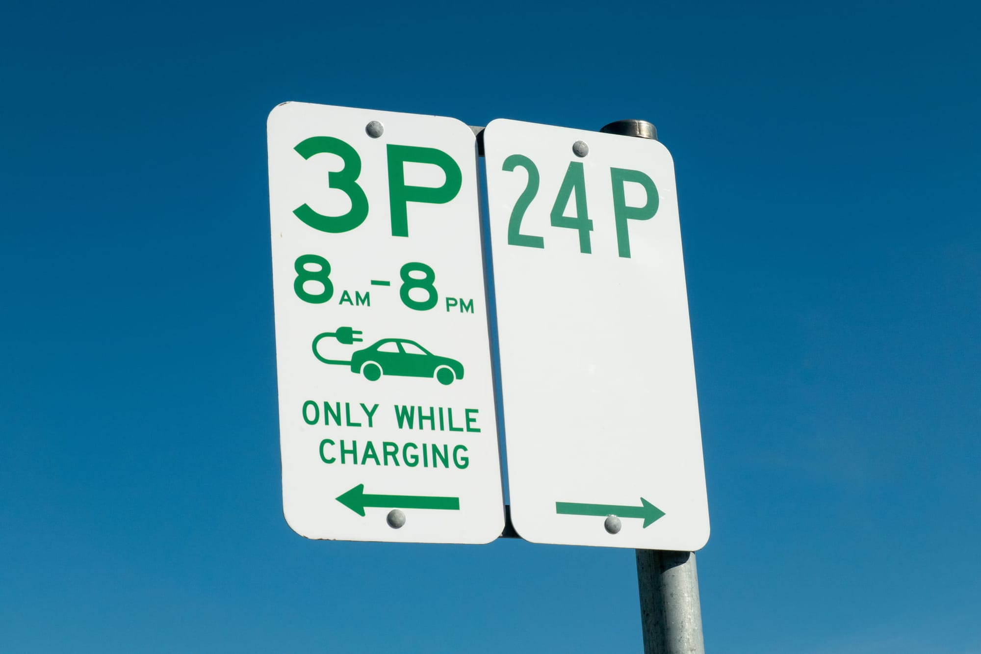 Parking signs, one on left reserving spaces for electric vehicles and time limits for charging, and on the right indicating unlimited parking time of 24 hours.