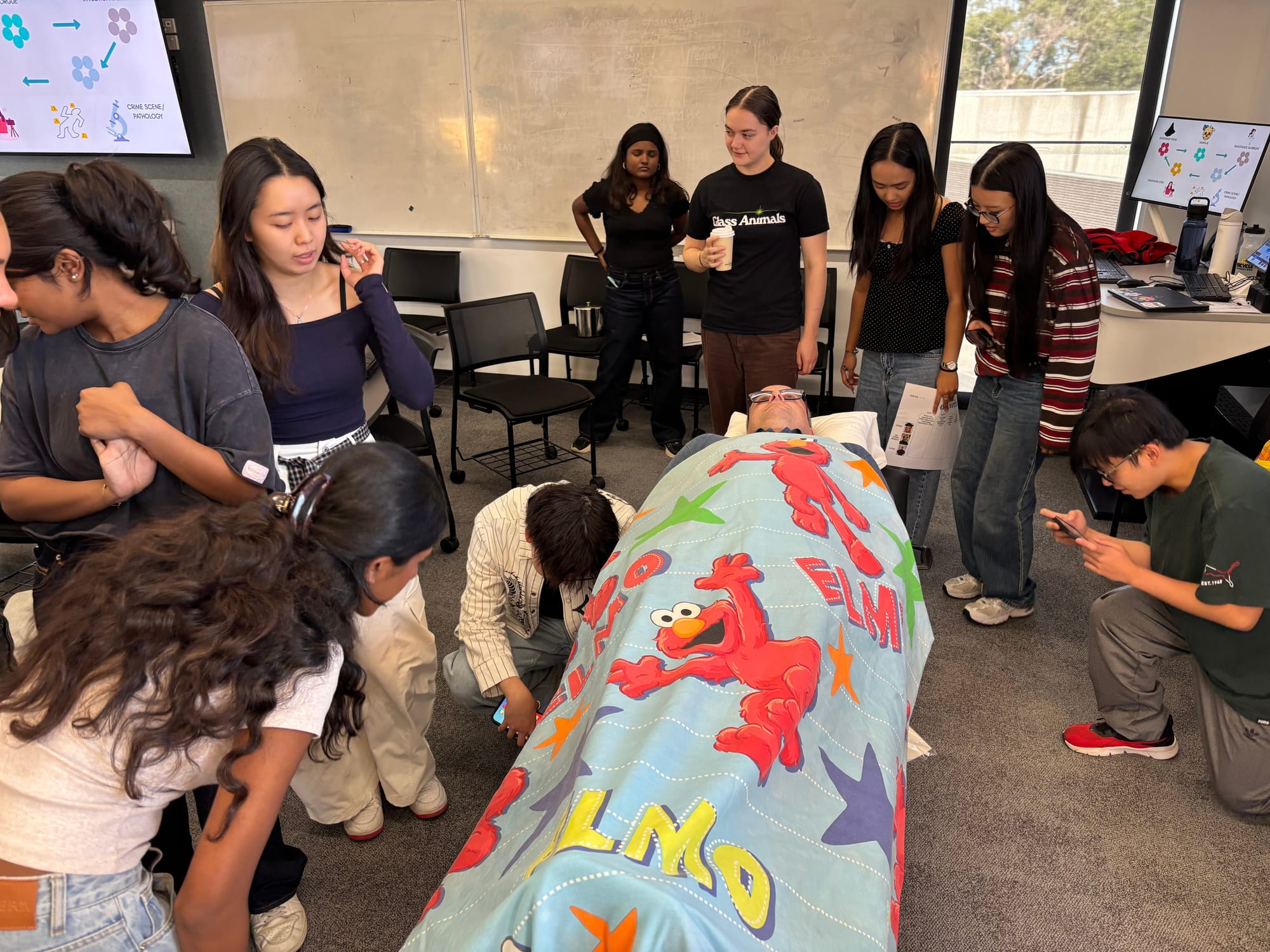 Students gather around a "body" covered by a blanket, examining clues