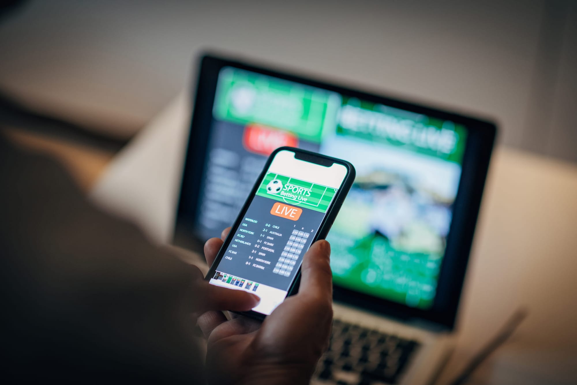 Man using mobile app for live betting and online gambling and watching a sports match