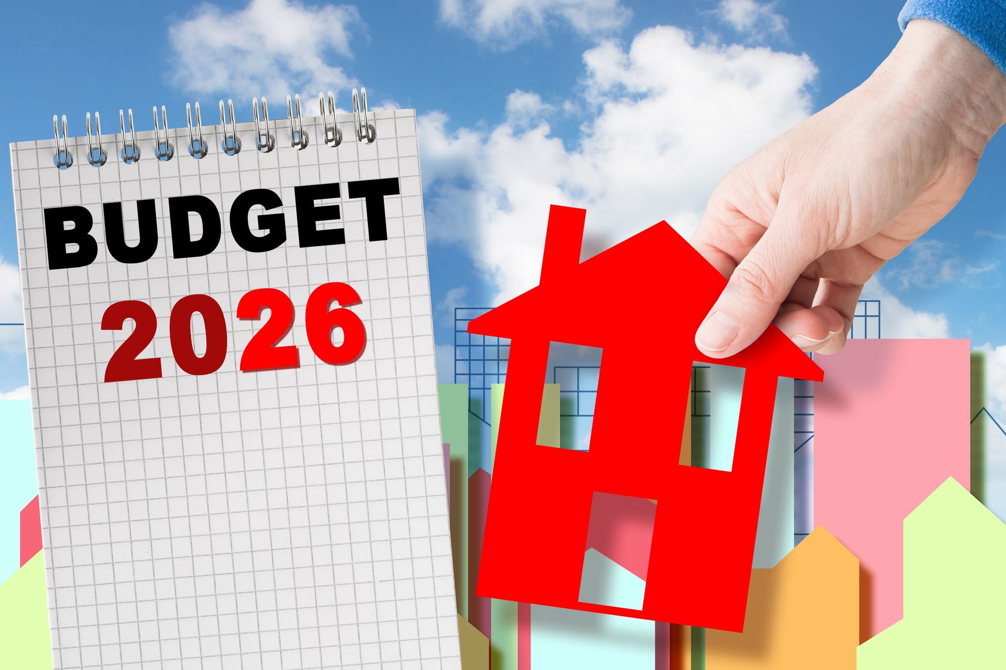 New house 2026 Budget concept. Person reaching for a red cardboard house. A notebook with Budget 2026 written on it.