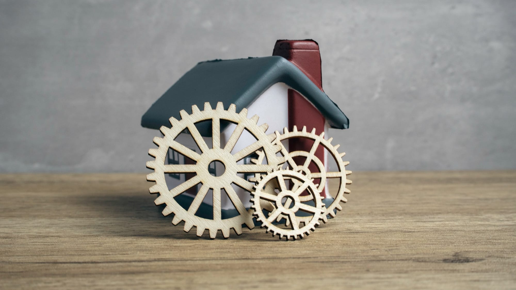 Wooden gears and cogs placed in front of a miniature toy house.
