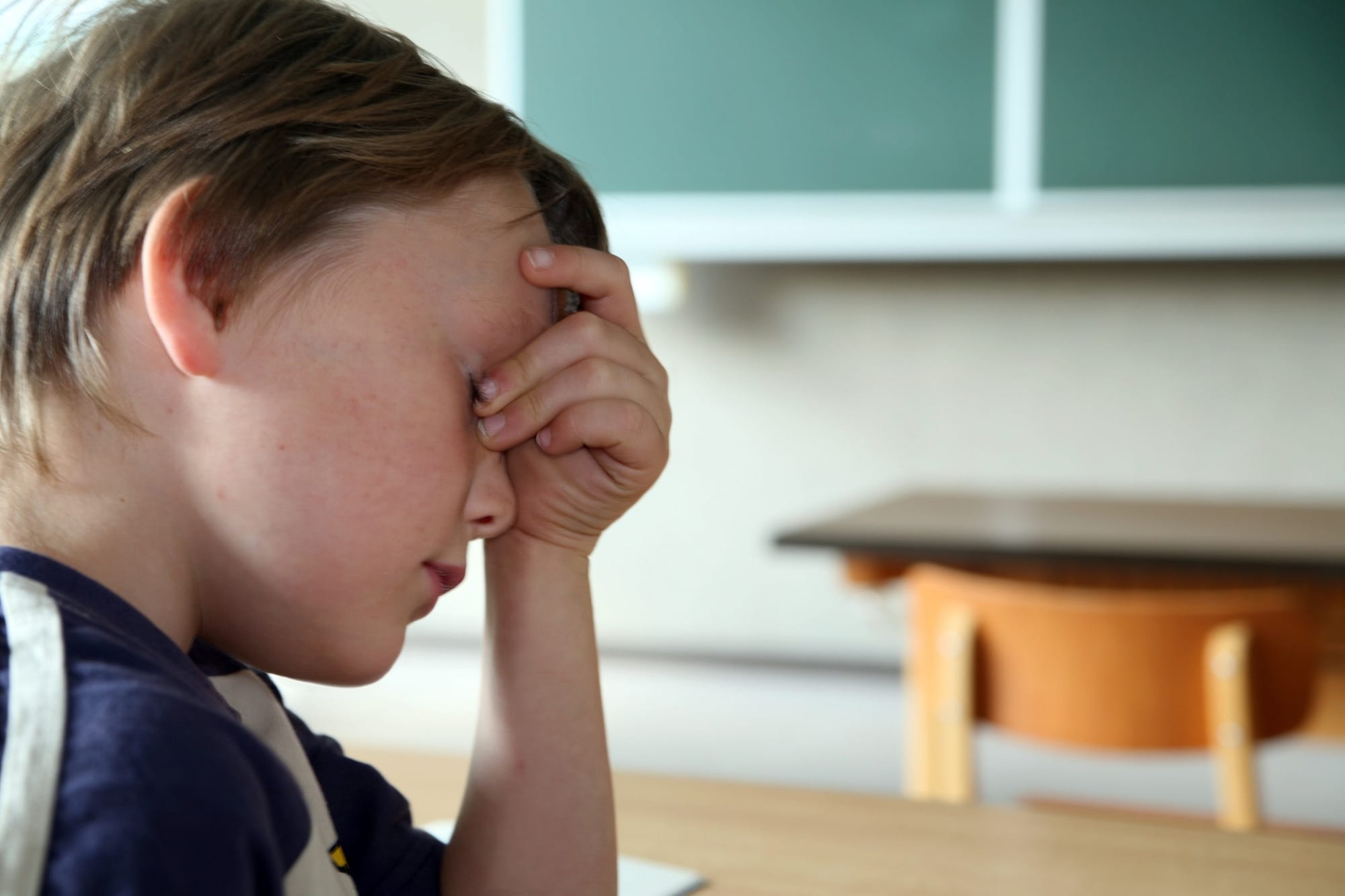 Child sitting in classroom with head in his hands.