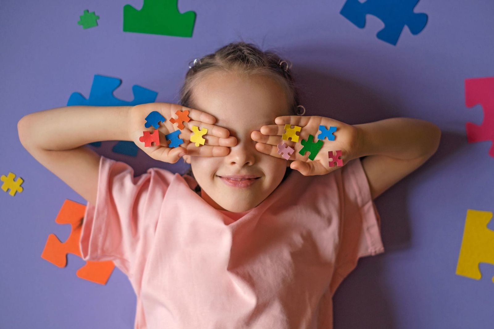 child holds colored puzzle pieces in her hands, closing his eyes. The generally accepted international symbol of autism
