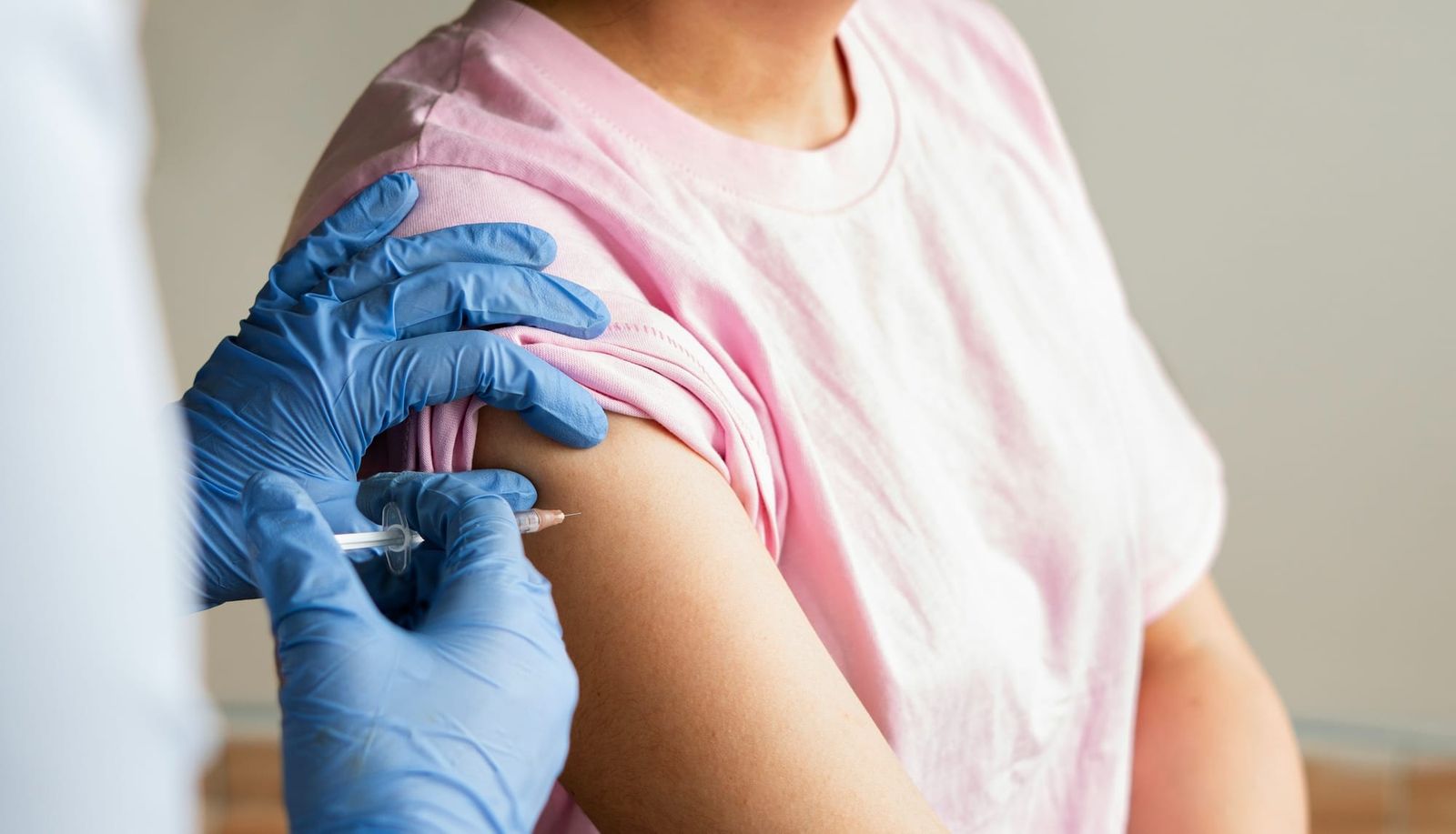 Person in blue medical gloves administering a vaccine or flu shot to a woman.